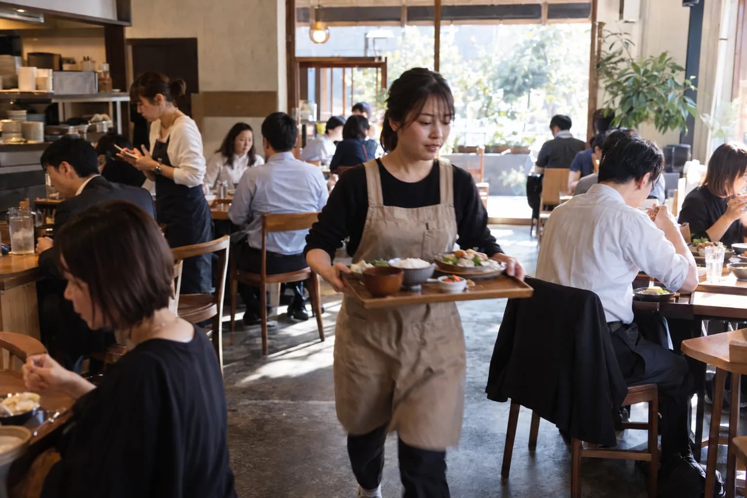 ランチタイムで満席の飲食店。スタッフが料理を運んでいる